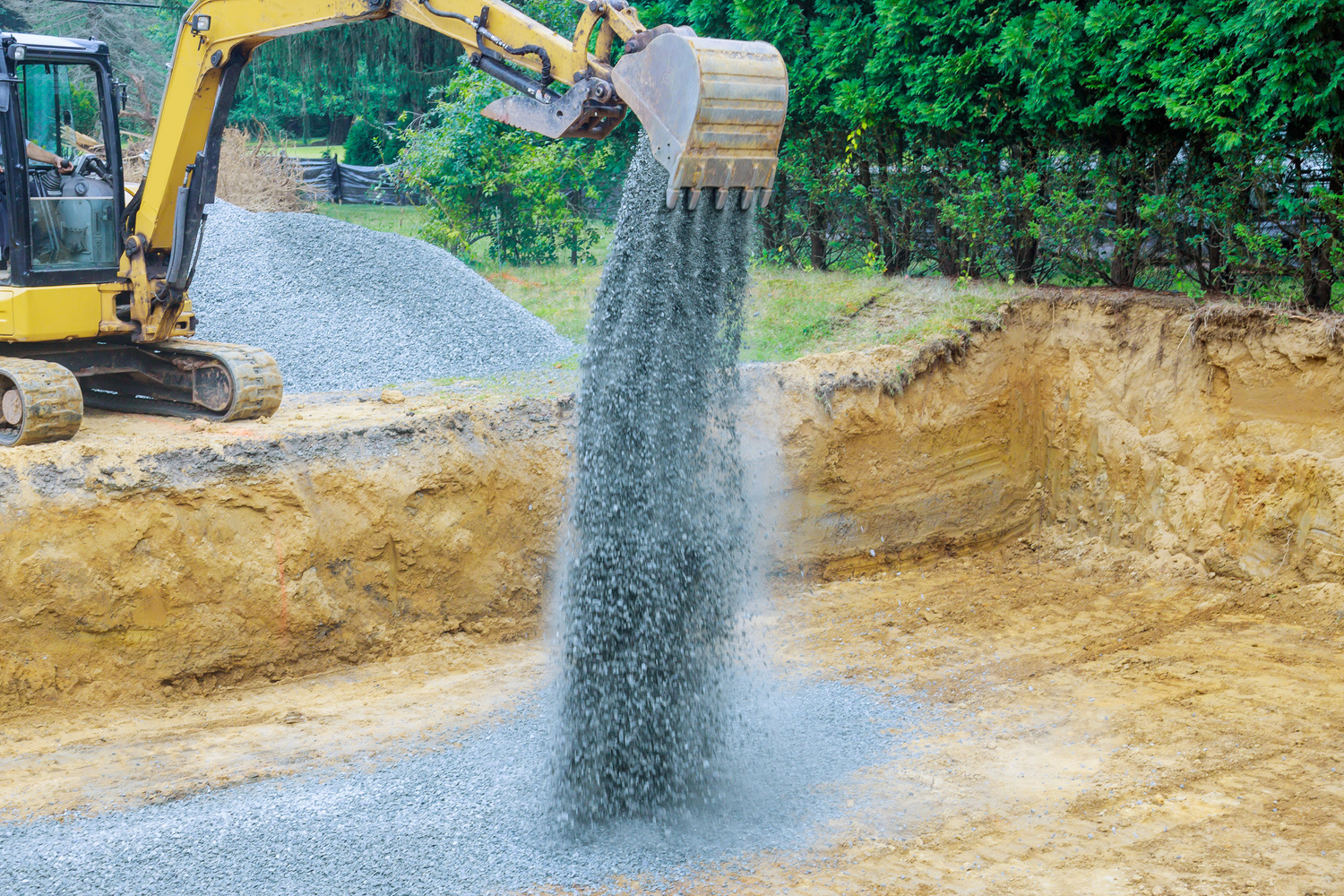 Excavator with a bucket lowered down gravel stones for construction of foundation